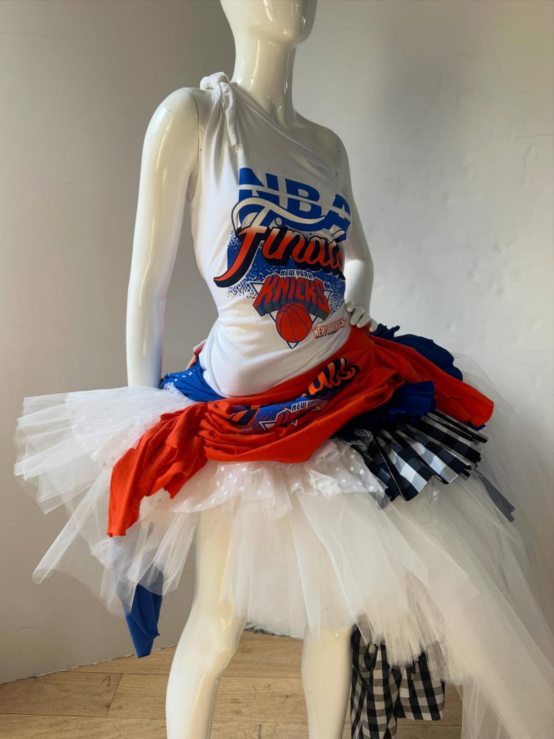 A mannequin displaying a custom outfit made from New York Knicks NBA Finals t-shirts draped and layered over a white tulle skirt with black gingham fabric accents.