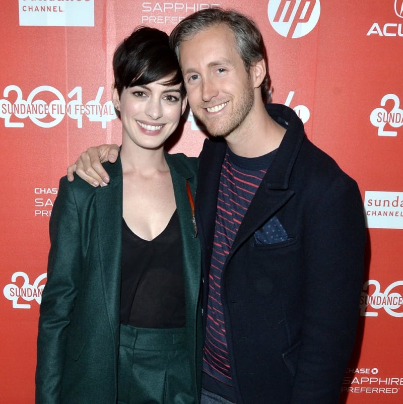 Anne Hathaway and Adam Shulman posing together at the 2014 Sundance Film Festival against a red branded backdrop.