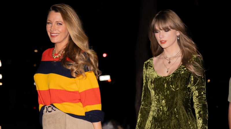Blake Lively and Taylor Swift standing together at night; Blake on left wears colorful striped sweater, Swift on right wears green velvet top.