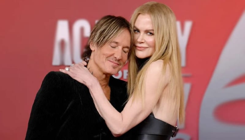 Two people embracing at a red carpet event with blurred text visible in the background.