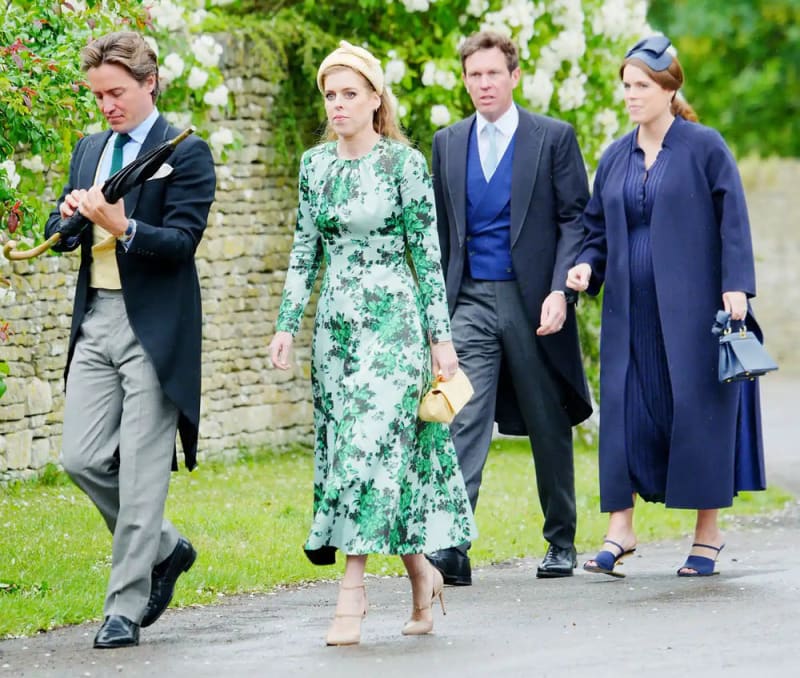 Two women and two men walking outdoors — one woman in a green floral midi dress and yellow headband, the other in a navy coat with a navy fascinator, accompanied by two men in morning suits.