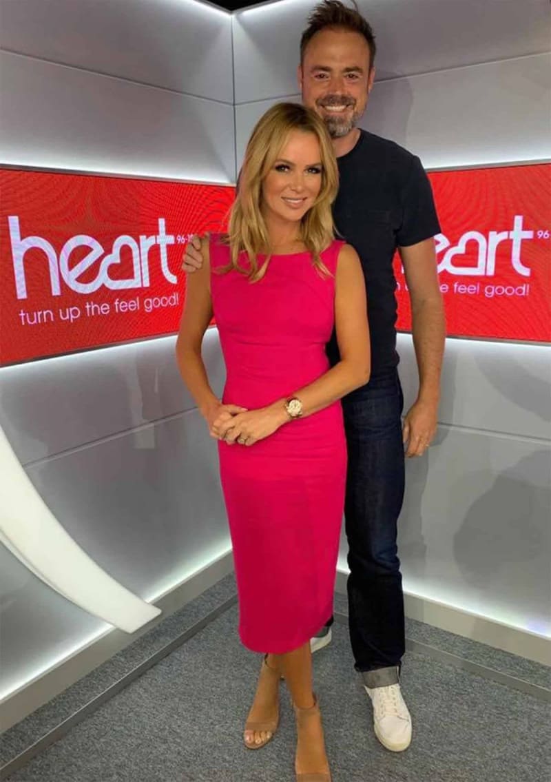 Two people posing together in front of Heart radio branding and signage in a studio setting.