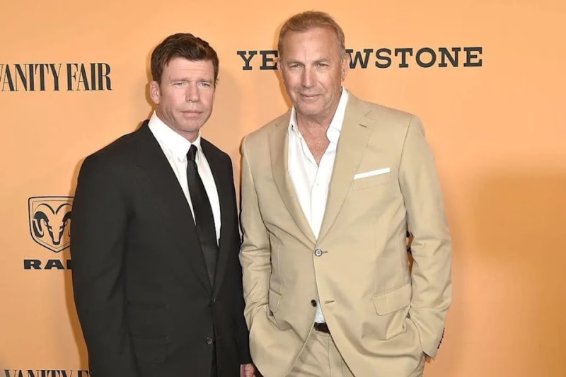 Two men in suits pose together at a Yellowstone premiere event with Vanity Fair branding visible in the background.