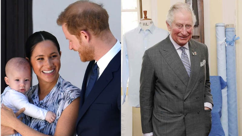 A woman in a blue and white patterned dress holds a baby in a white babygrow while a red-haired man in a dark suit looks on smiling, alongside an older man in a grey double-breasted suit standing before fabric rolls and a tailor's dummy.