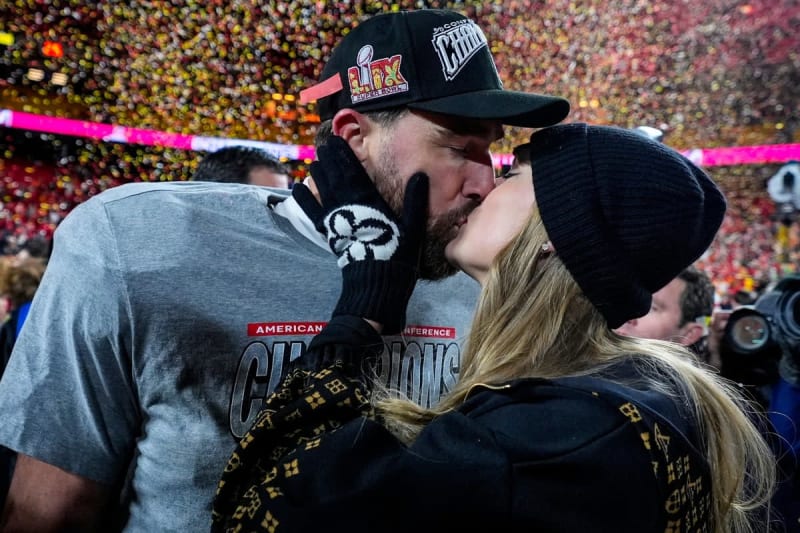 A couple kisses on the field after an AFC Championship game, with confetti falling in the background.