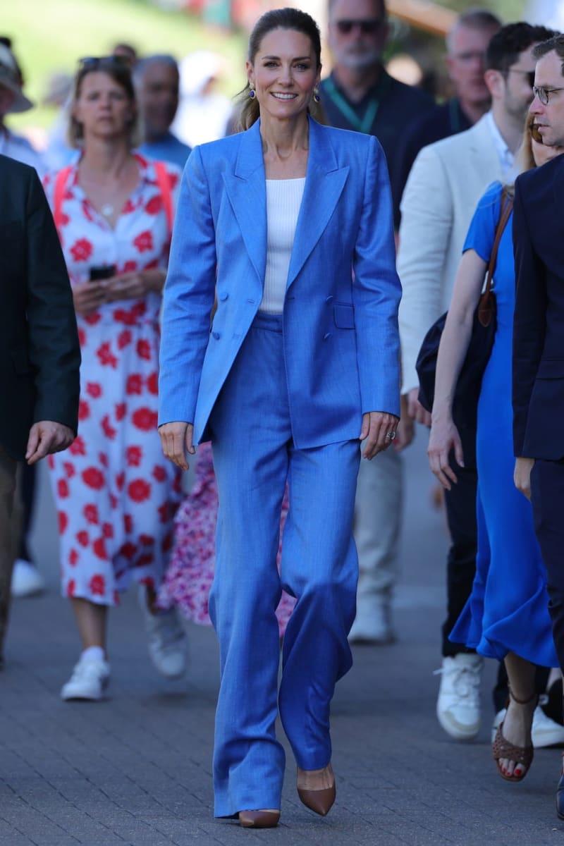 A woman in a bright blue linen suit and white top walks smiling through a crowd at an outdoor event.