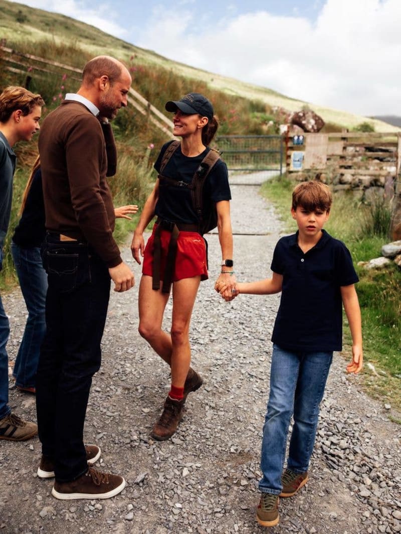 A group of people having a conversation on a rural gravel path with green hillsides in the background.