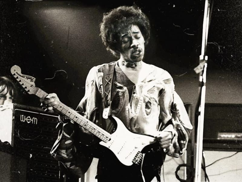 Black and white photograph of a musician with an afro hairstyle playing an electric guitar on stage during a performance.