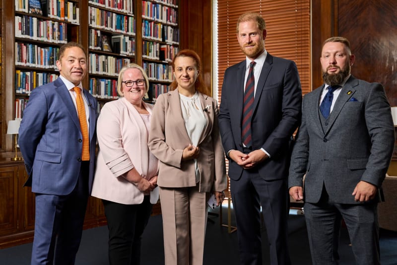 Five professionally dressed people standing together in a library, smiling at the camera.