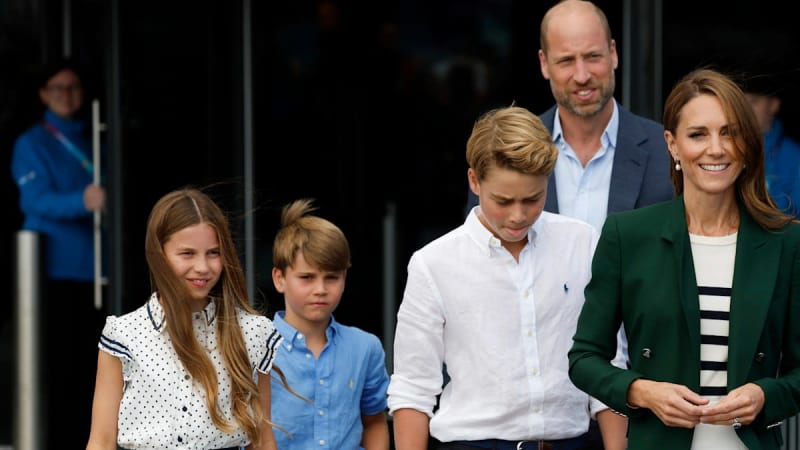 A family of five exits a building together, with adults and children dressed in smart casual attire on a sunny day.