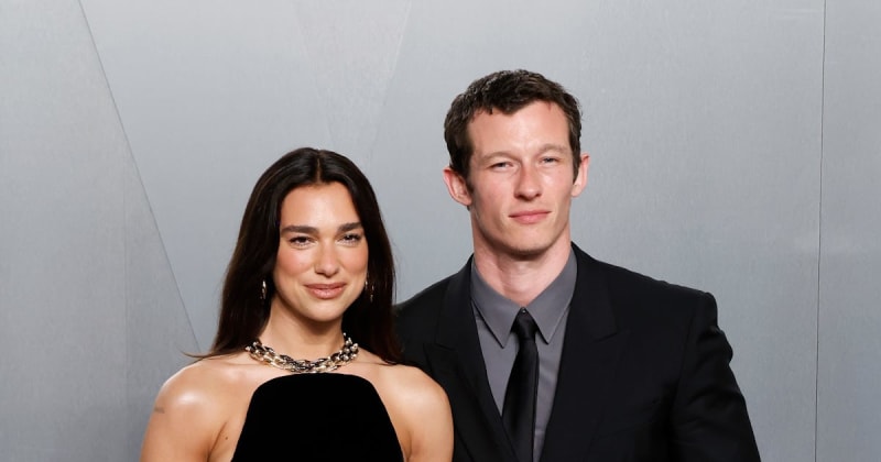 Two people posing together against a gray background at what appears to be a formal event or photo session.