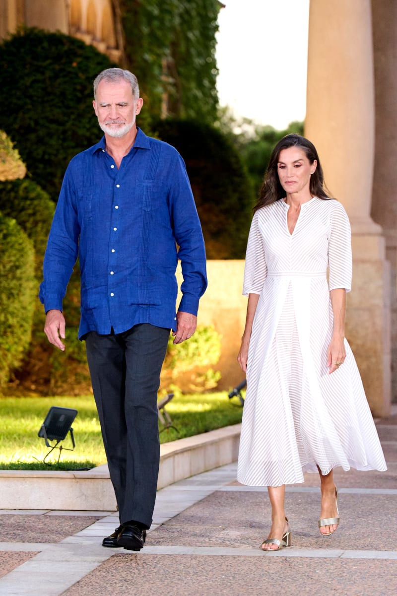 Two people walking together on a paved path in front of a building with ivy and manicured gardens.