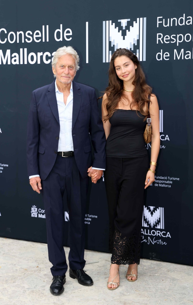 Two people pose together at a Mallorca tourism event, with the man wearing a dark suit and the woman in black attire.