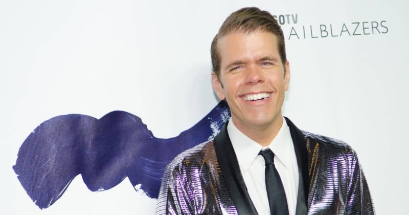 A man in a sequined purple and black jacket smiles at a media event with "Trailblazers" branding visible behind him.