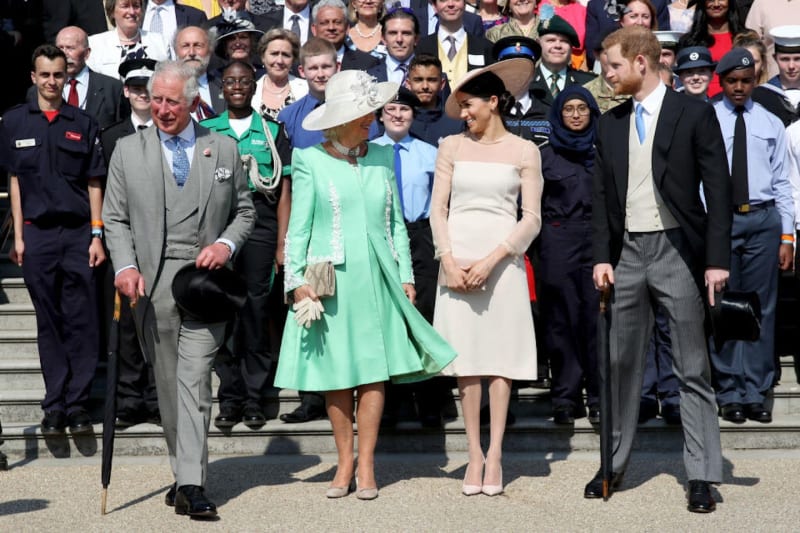 A formal outdoor gathering with dignitaries in ceremonial dress, including a woman in a green coat and another in a cream dress.
