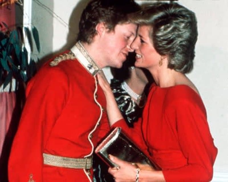Two people in red outfits with decorative trim embracing and smiling at each other at what appears to be a formal event.