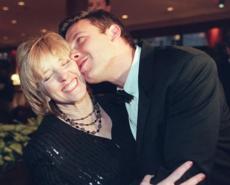 Woman in black top laughing as man in dark suit kisses her cheek, indoor event.