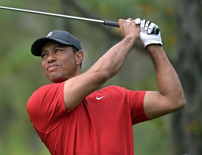 Man in red Nike shirt and black cap mid-golf swing outdoors.