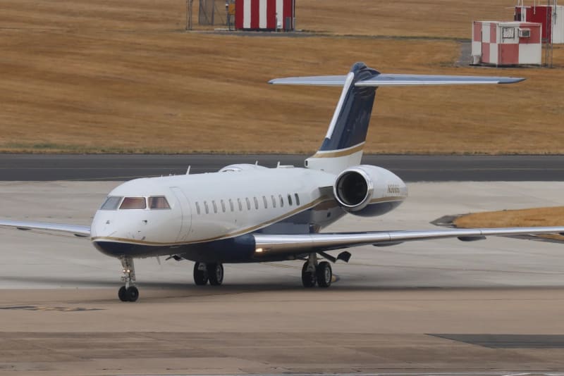 White and navy private jet with gold trim taxiing on airport runway.