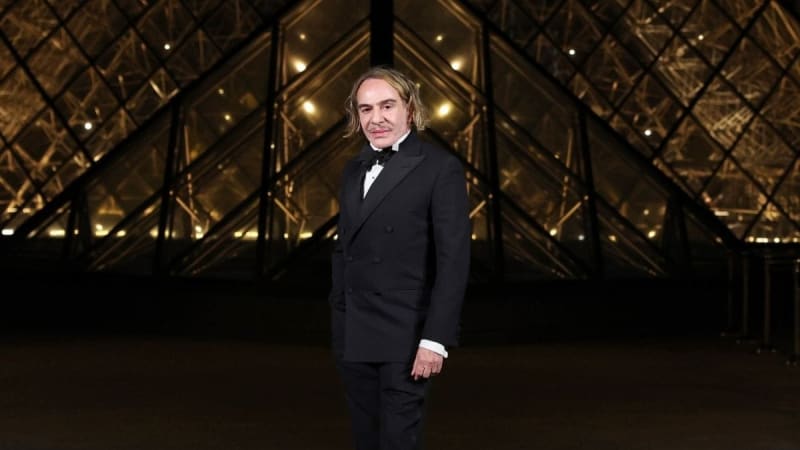 A man in a black tuxedo and bow tie stands in an elegant corridor with gold geometric latticed walls and warm lighting.