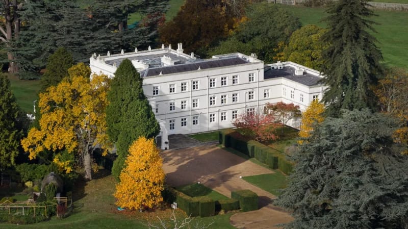 Aerial view of a white neoclassical mansion surrounded by autumn foliage and manicured gardens.