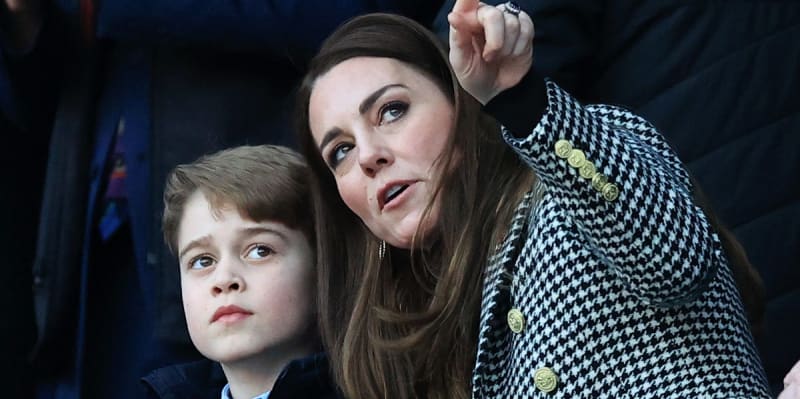 A woman in a black and white houndstooth jacket sits with a young child at what appears to be a public event.