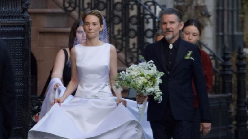 Woman in white wedding dress and veil holding bouquet, man in dark suit behind her, urban steps setting.