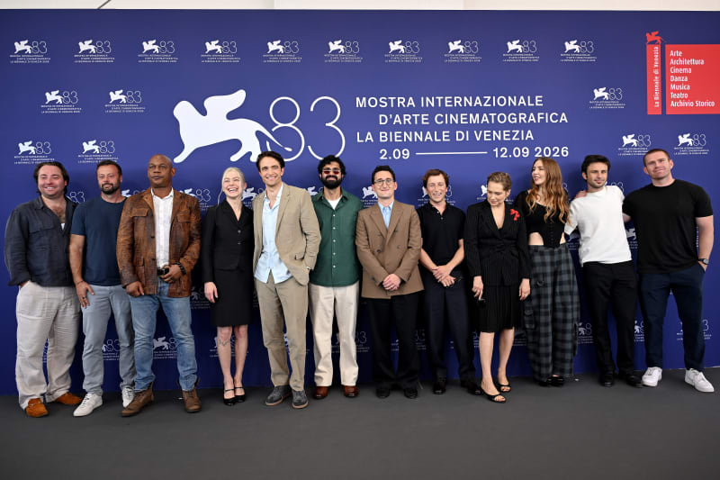 A group of eleven people stand in a line at the Venice Film Festival 83 photo call, posed against a blue backdrop.