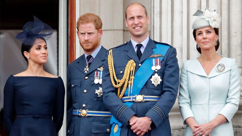 Four people in formal attire stand on a palace balcony; two men wear military dress uniforms with medals and decorations.