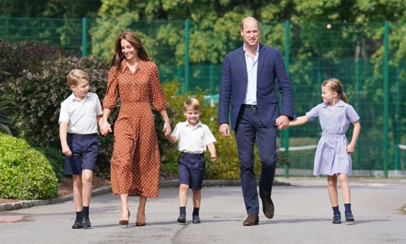 A family of five walks together on a school path, with two adults and three children in uniform attire.