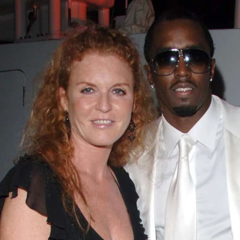 Woman in black dress and man in white suit with sunglasses, posing together at an indoor event.