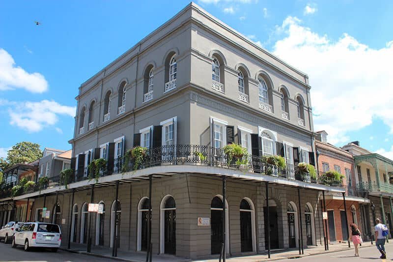 Three-storey grey building with iron balconies and arched windows on a French Quarter street corner.