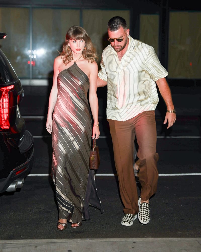 Woman in striped halter gown and man in striped shirt walking through parking lot at night.