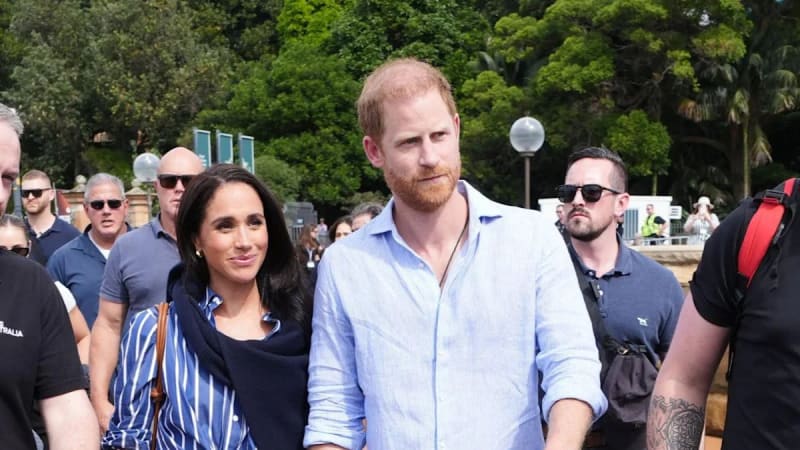 Woman in blue striped top and man in light blue shirt walking together outdoors with crowd behind them.