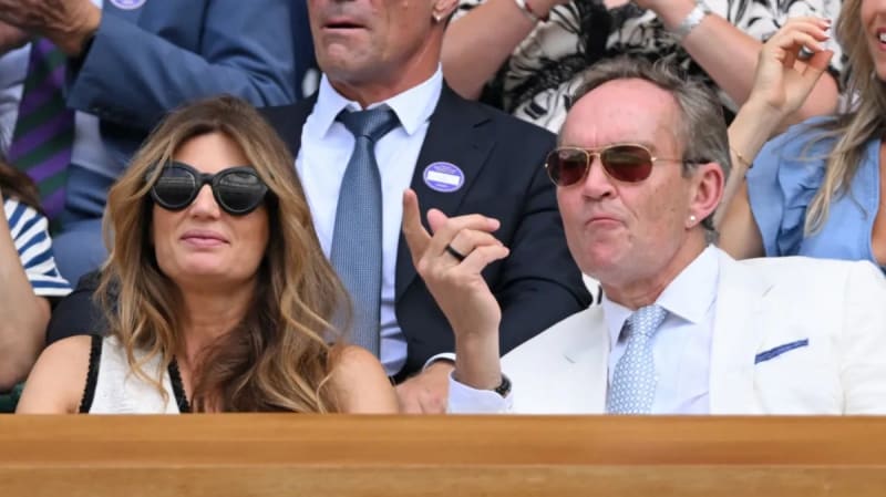 Two spectators wearing sunglasses sit in a viewing box at what appears to be a sporting event or tournament.
