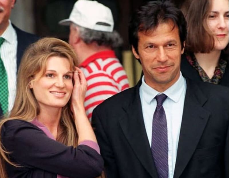 Woman in purple top touching hair beside man in black suit and tie, crowd behind.