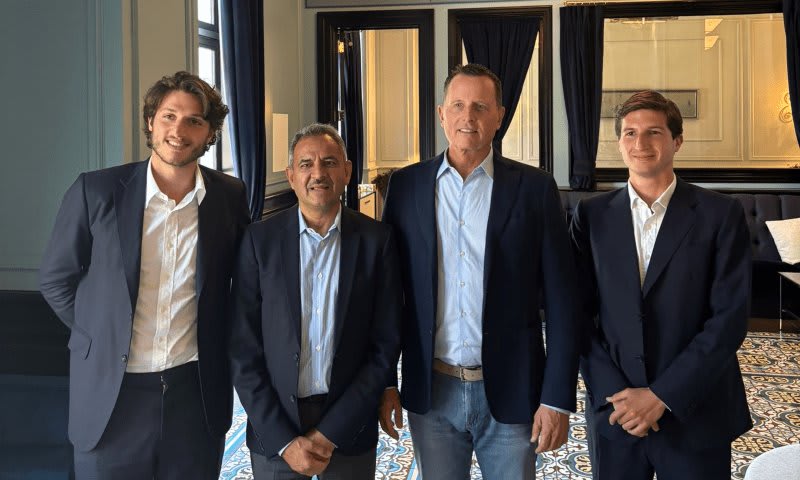 Four men in suits and blazers posing indoors, tiled floor visible.