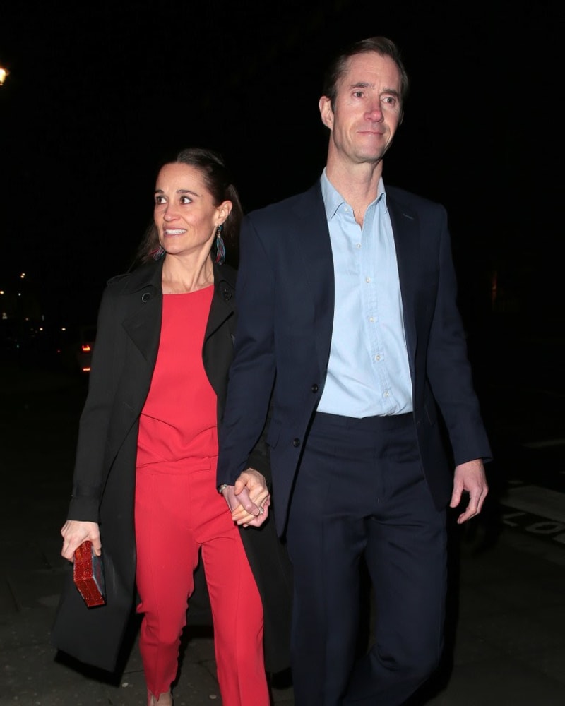 Two people holding hands while walking together at night, woman in red outfit with black blazer, man in dark suit and light blue shirt.