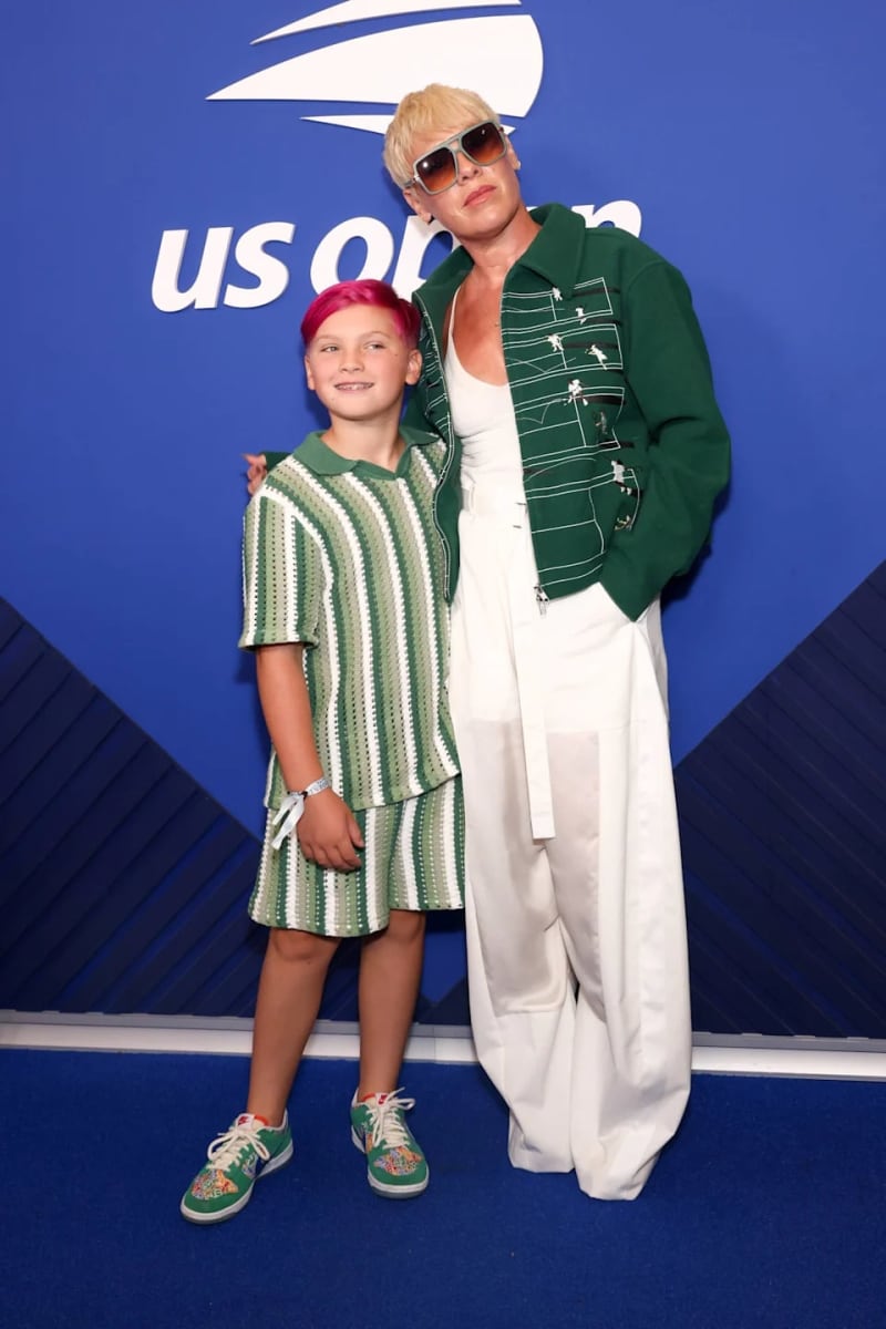 Two people in coordinated green and white outfits pose together at a US Open event against a blue backdrop.