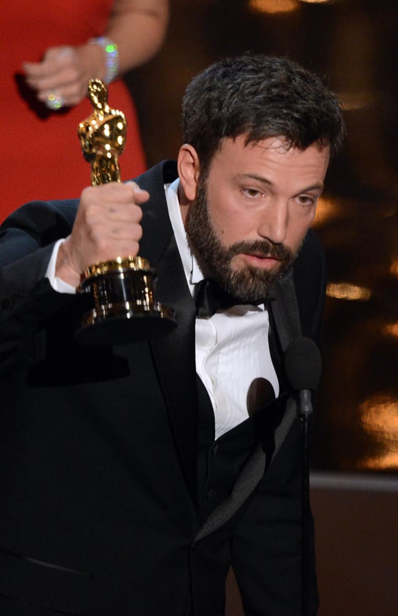 Man in black tuxedo holding Oscar statuette at podium.