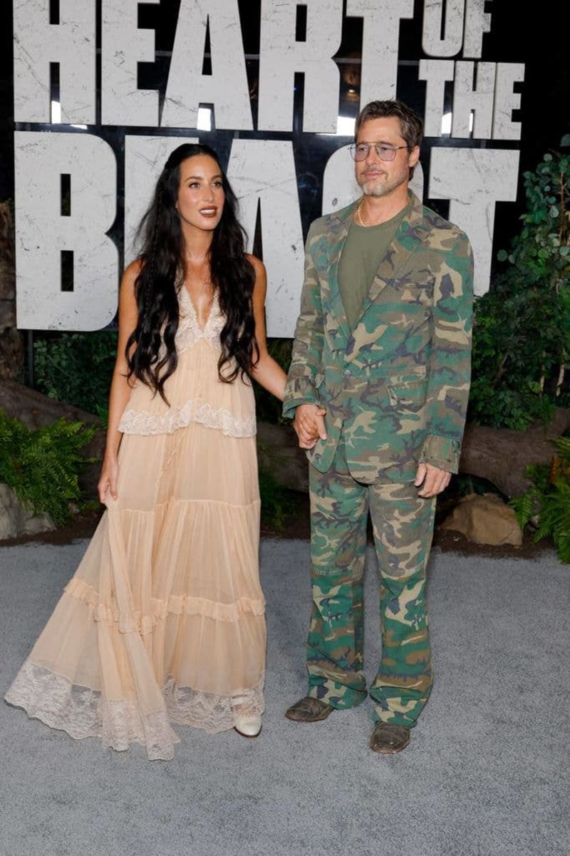 Two people posing together at a "Heart of the Beast" event, with the woman wearing a cream lace dress and the man in camouflage attire.
