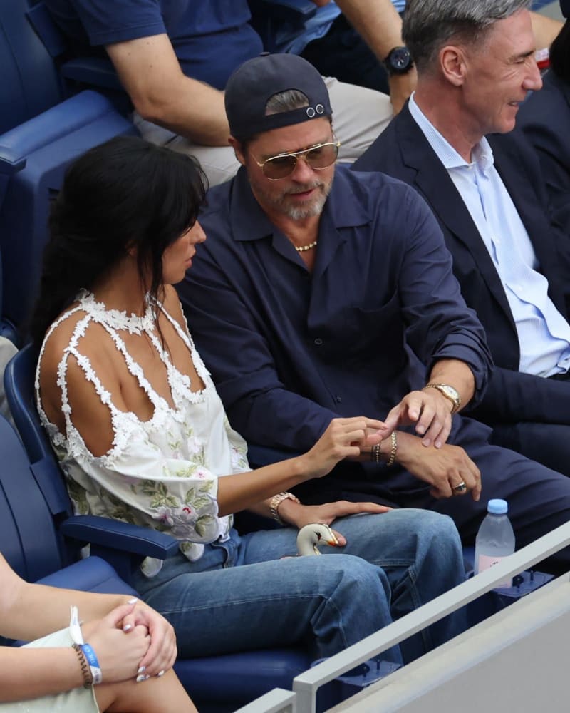Woman in white floral top and man in navy shirt with backwards cap, seated in stadium stands.