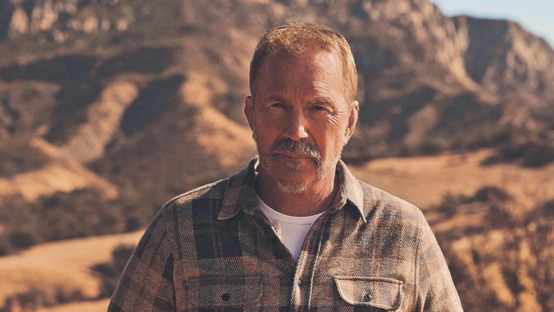 A middle-aged man with a mustache wearing a tan shirt stands in front of desert mountains during golden hour.
