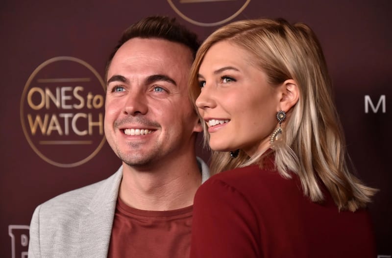 Two smiling people at a red carpet event with "ONEStoWATCH" branding visible in the background.