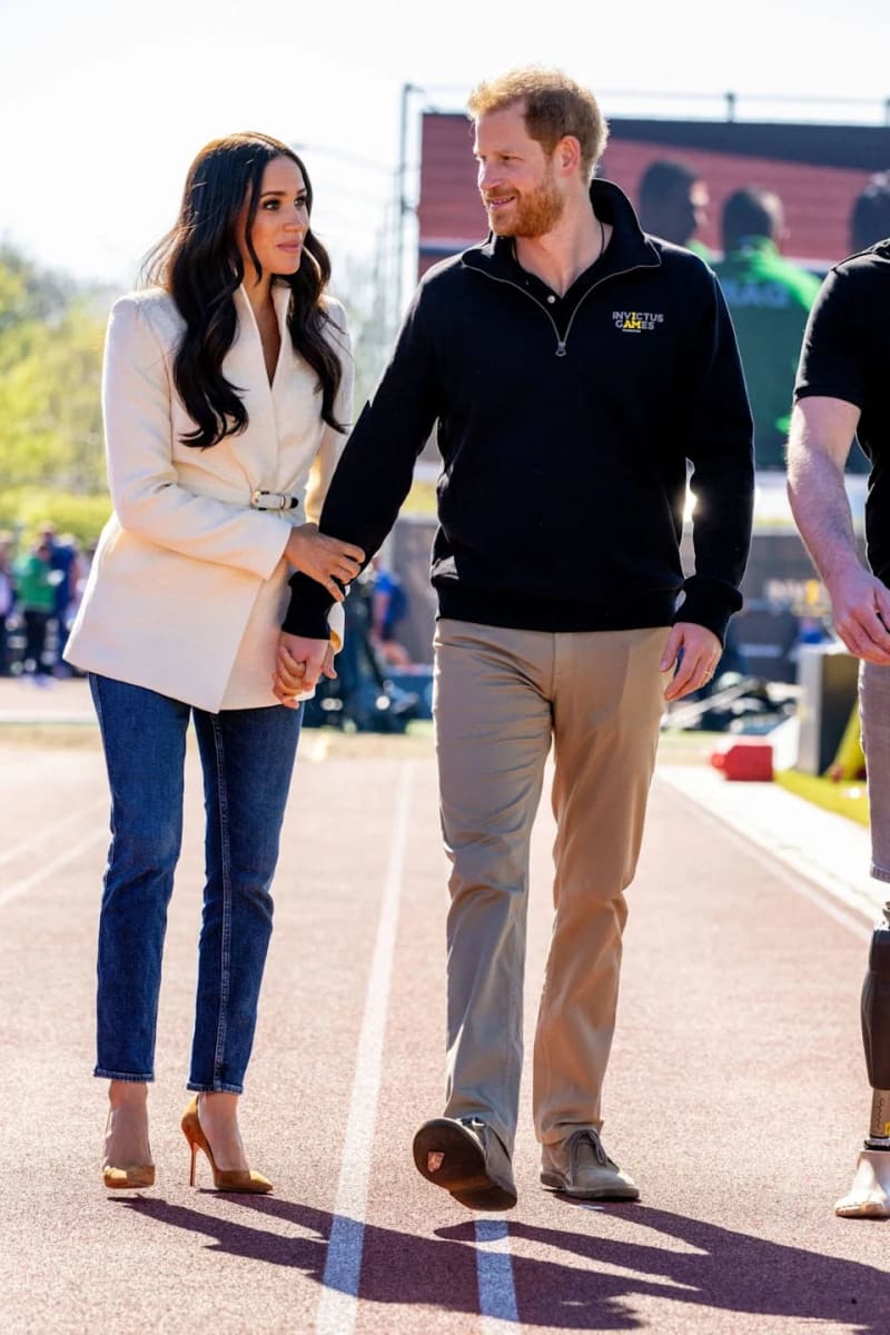 Two people walking together at an outdoor sporting event, the woman wearing a cream blazer and jeans, the man in a black jacket.