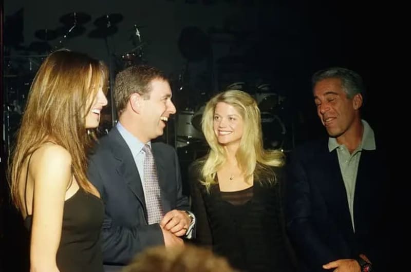Four people in formal attire conversing at an indoor event with stage lighting visible in the background.