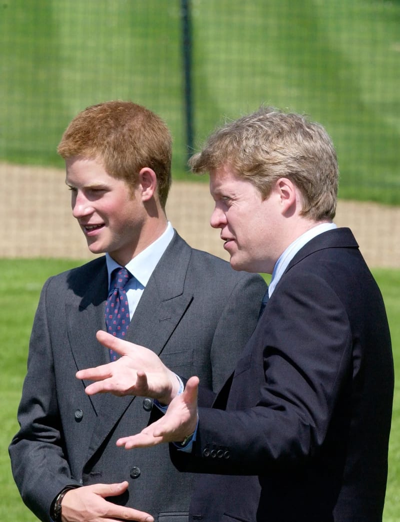 Two males in dark suits conversing outdoors on grass.