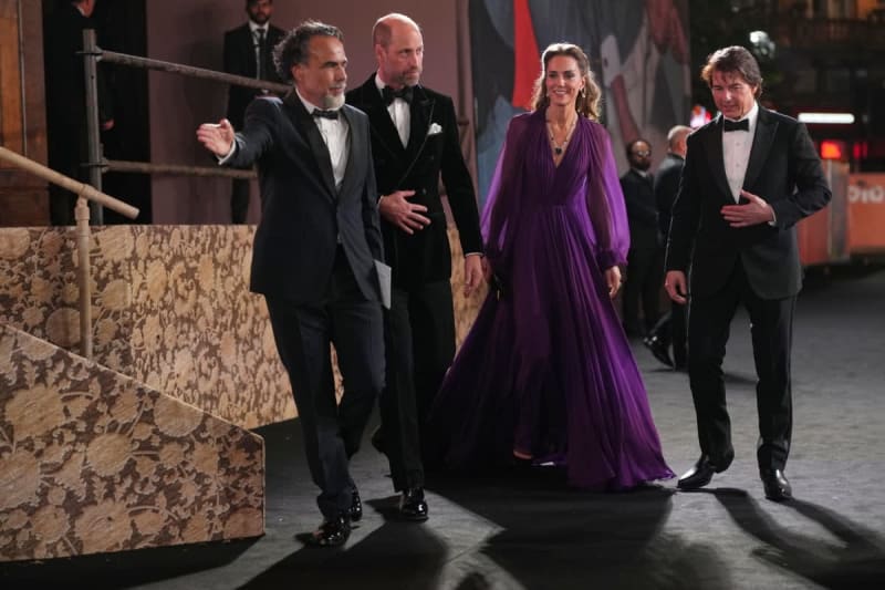 Four elegantly dressed people in formal attire walk together at what appears to be an upscale event or premiere.