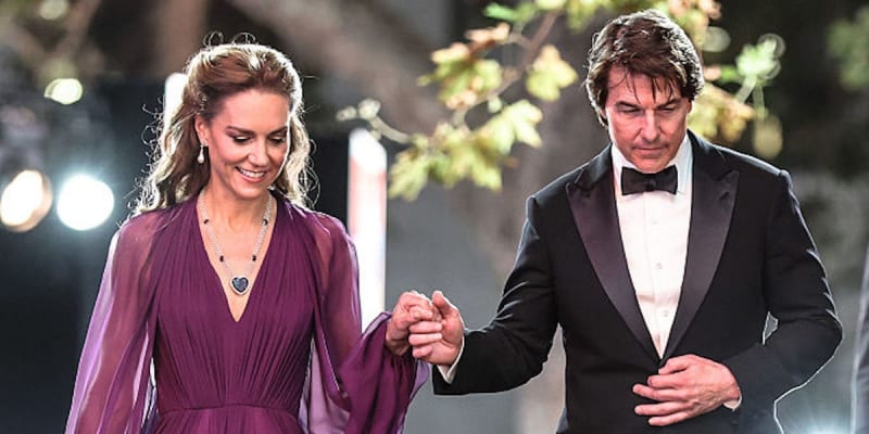 A man in a black tuxedo and a woman in a burgundy dress walk together arm-in-arm at night.