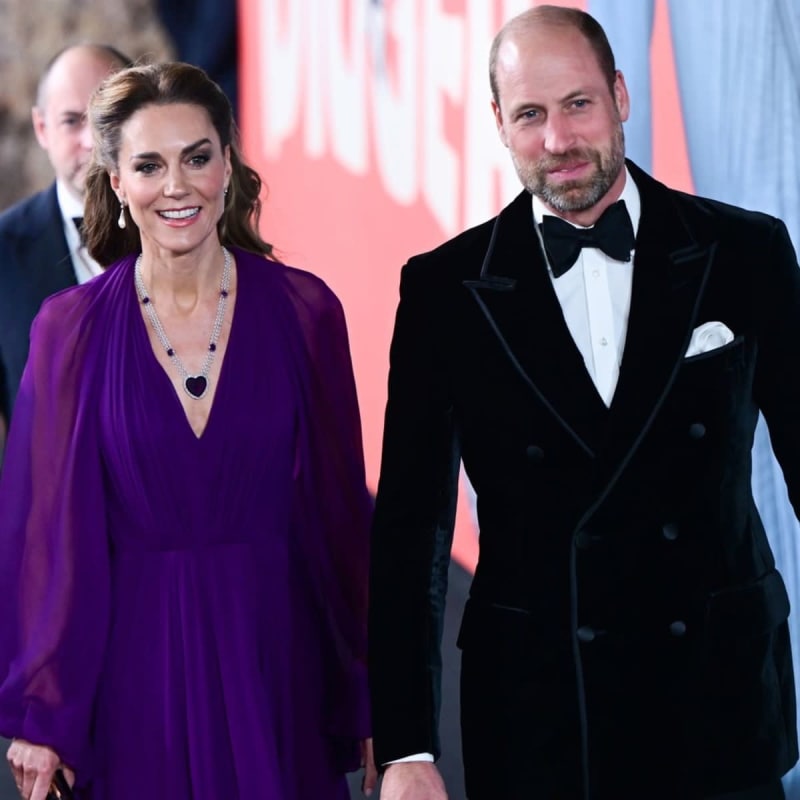 Two people in formal evening wear walk together on a red carpet at an elegant event.